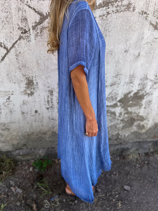 Woman wearing the Dolores™ flowing V-neck dress with short sleeves, standing relaxed in warm sunlight.