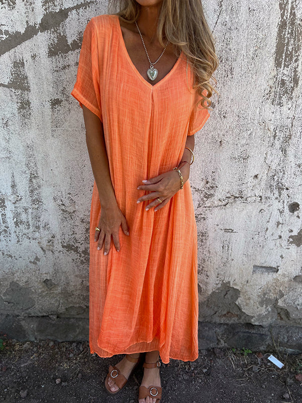Woman wearing the Dolores™ flowing V-neck dress with short sleeves, standing relaxed in warm sunlight.
