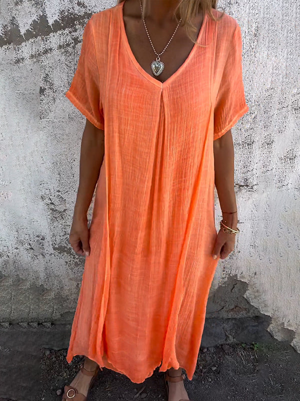 Woman wearing the Dolores™ flowing V-neck dress with short sleeves, standing relaxed in warm sunlight.