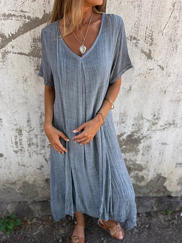 Woman wearing the Dolores™ flowing V-neck dress with short sleeves, standing relaxed in warm sunlight.