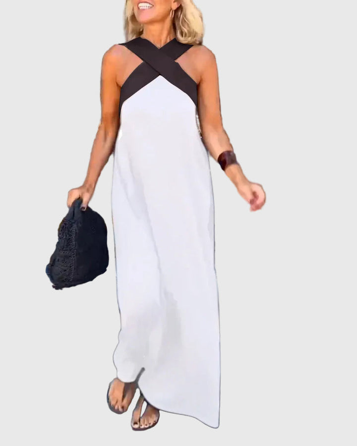 Woman wearing the Mary halterneck maxi dress in navy with a contrast crossover neckline, walking outdoors.