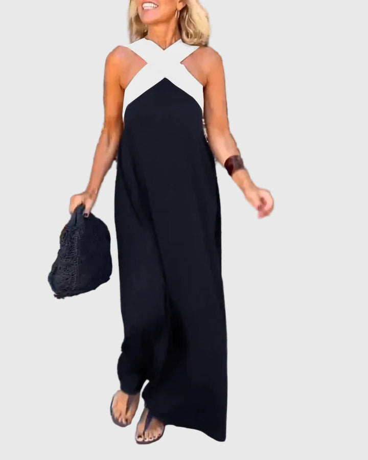 Woman wearing the Mary halterneck maxi dress in navy with a contrast crossover neckline, walking outdoors.