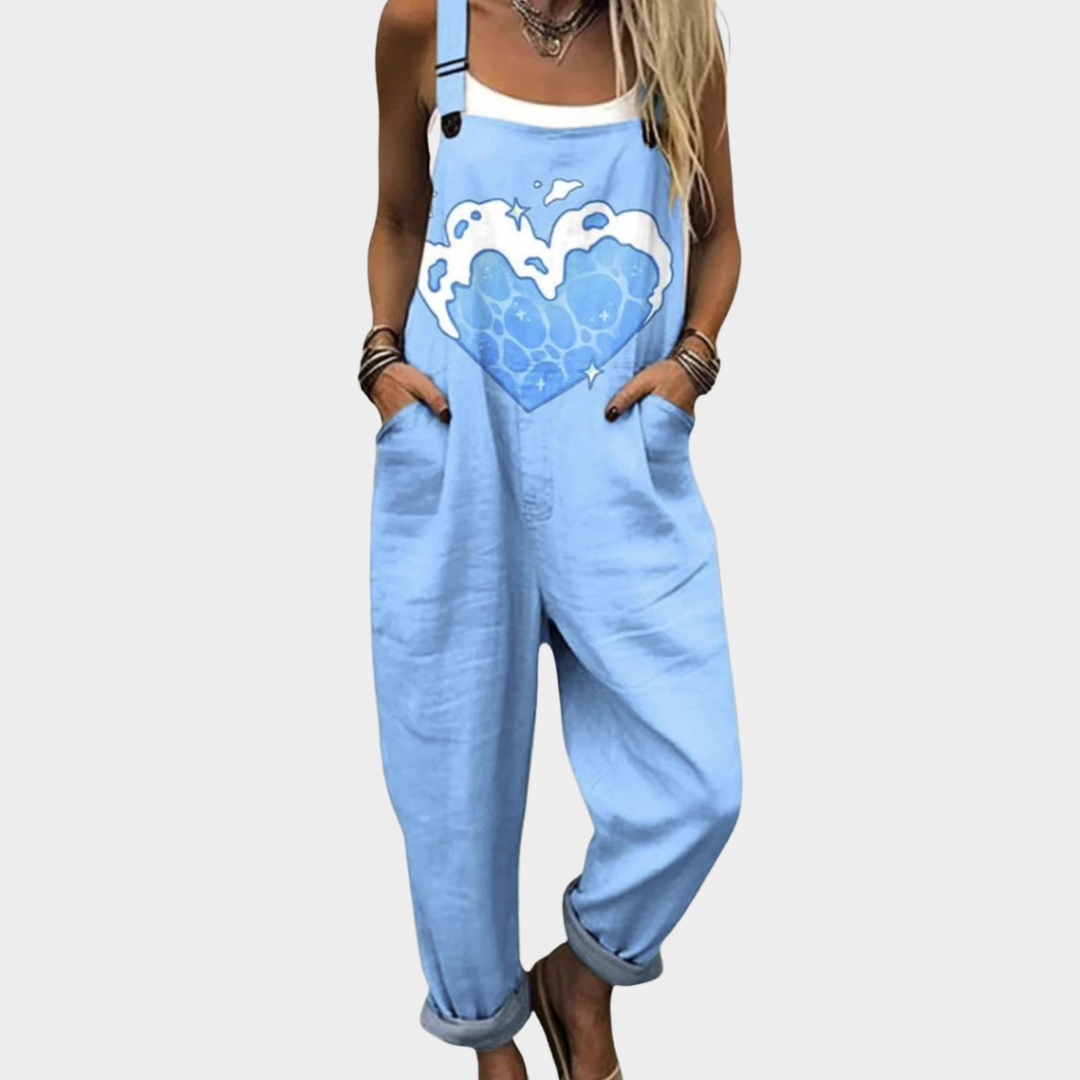 Woman wearing light blue dungarees with a large heart and cloud print, adjustable straps, cheerful and relaxed.
