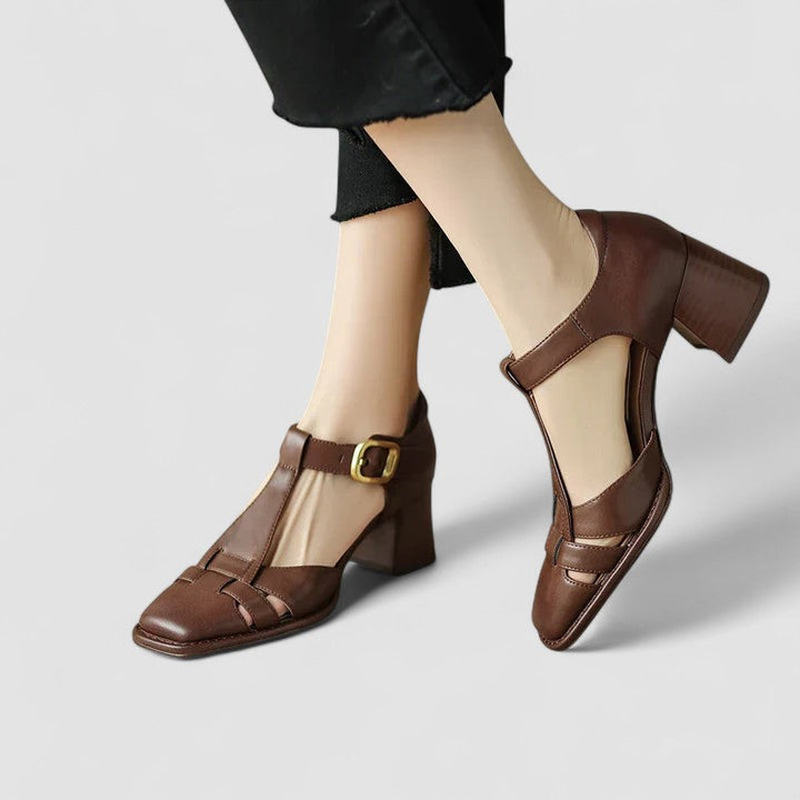 A woman wearing beige t-strap block heel sandals with an adjustable buckle, standing comfortably.