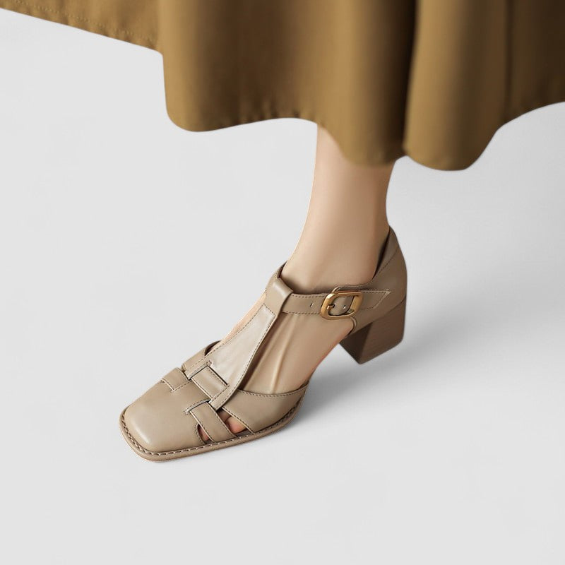 A woman wearing beige t-strap block heel sandals with an adjustable buckle, standing comfortably.
