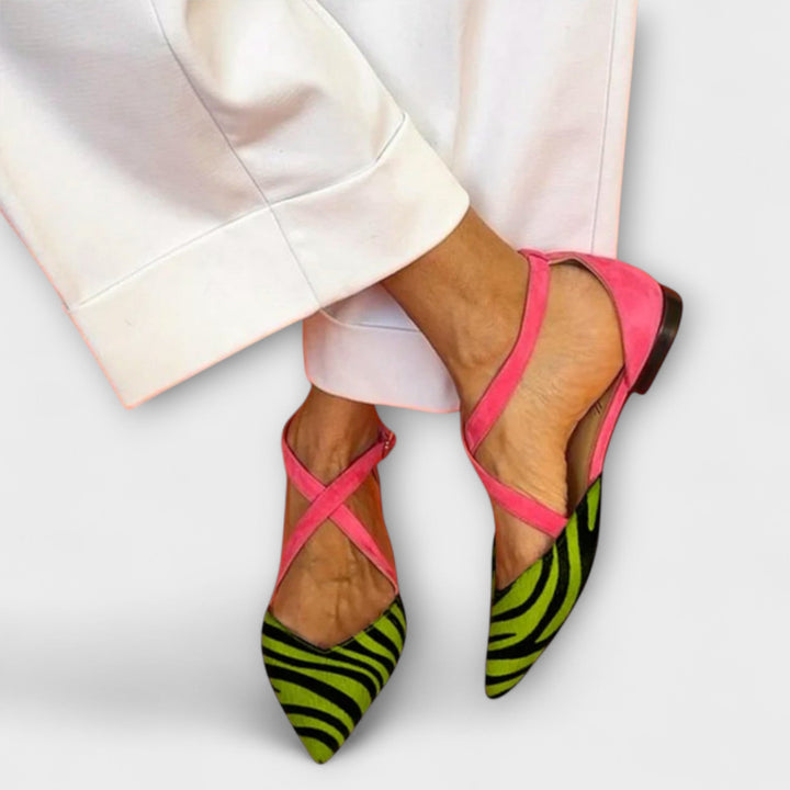 A woman wearing pointed flats with a zebra-print toe and pink cross-over ankle straps.