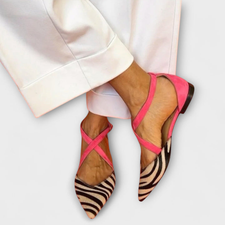 A woman wearing pointed flats with a zebra-print toe and pink cross-over ankle straps.