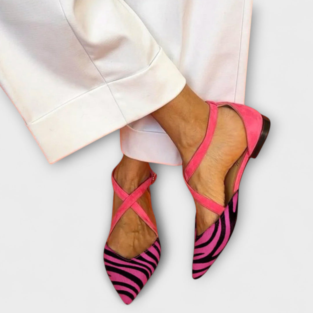 A woman wearing pointed flats with a zebra-print toe and pink cross-over ankle straps.