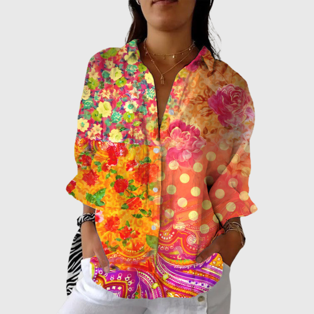 A woman wearing a flowing floral printed blouse with trousers, smiling outdoors