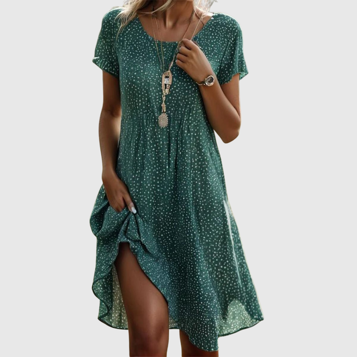 Woman wearing the Amy speckled summer dress in green, smiling in the sunshine outdoors.