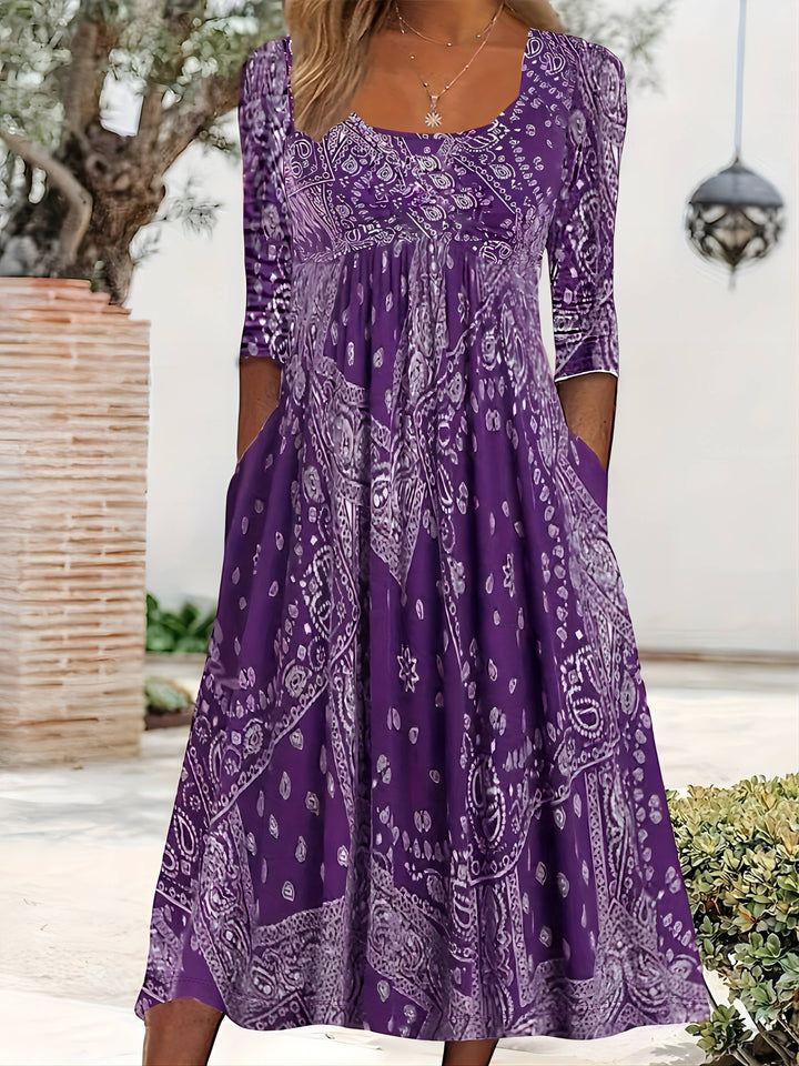A woman wearing the Maureen long sleeve grey paisley midi dress with a square neckline and flowing skirt, styled for a relaxed day out.