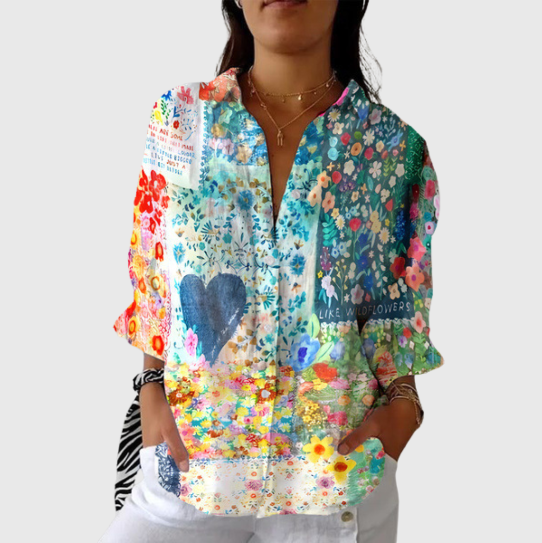 A woman smiling in a bright floral printed blouse, worn loose with trousers