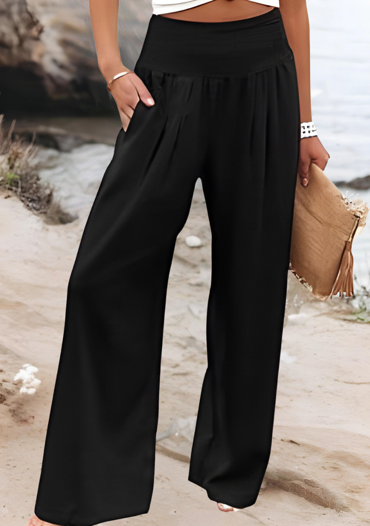 A woman walking by the sea in wide-leg beach trousers with a relaxed, breezy summer look.