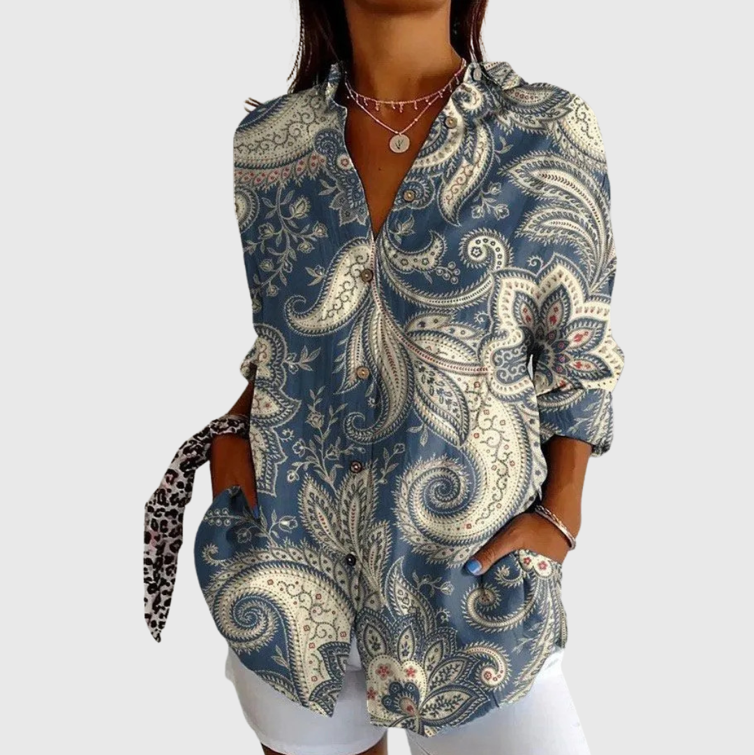 A woman wearing a relaxed colourful printed blouse with adjustable sleeves, styled with trousers for an easy day out.