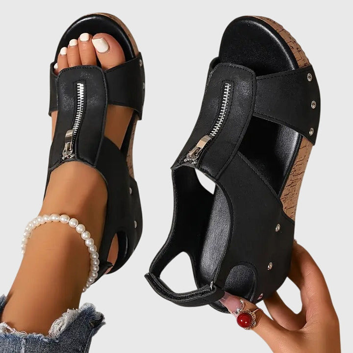 A woman wearing black zip-front wedge sandals with a cushioned footbed and open toe.