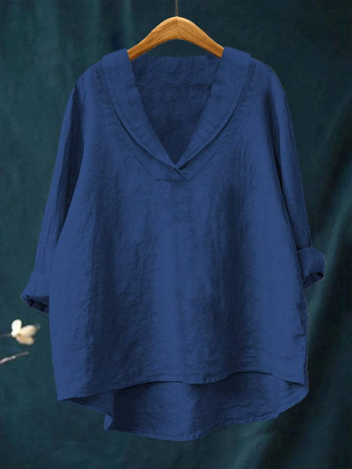 A woman wearing an elegant plain summer blouse with a flowing drape, styled with trousers.