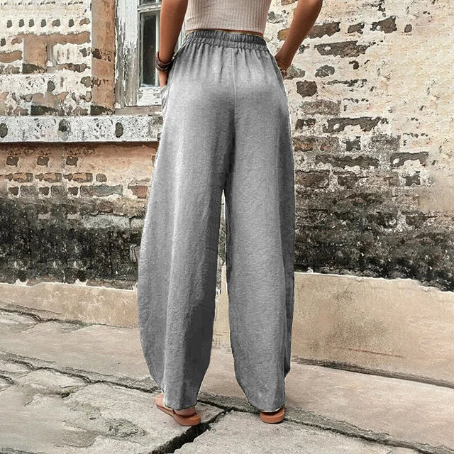 A woman walking in flowing wide-leg trousers with big patch pockets and an elegant, draped silhouette.