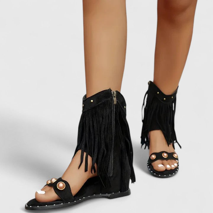 A woman wearing black fringe-detail sandals with a cushioned sole and adjustable strap.