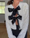 White shimmer blazer with large black bow detail and a cropped, structured cut