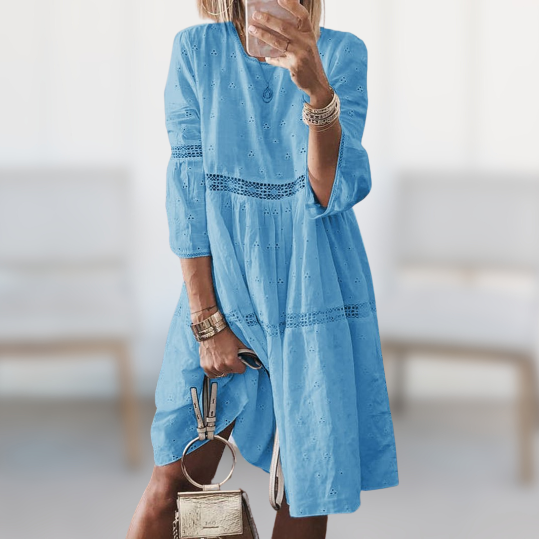 Woman wearing the Majella™ elegant summer dress with a round neckline and flowing silhouette, standing outdoors on a sunny day.