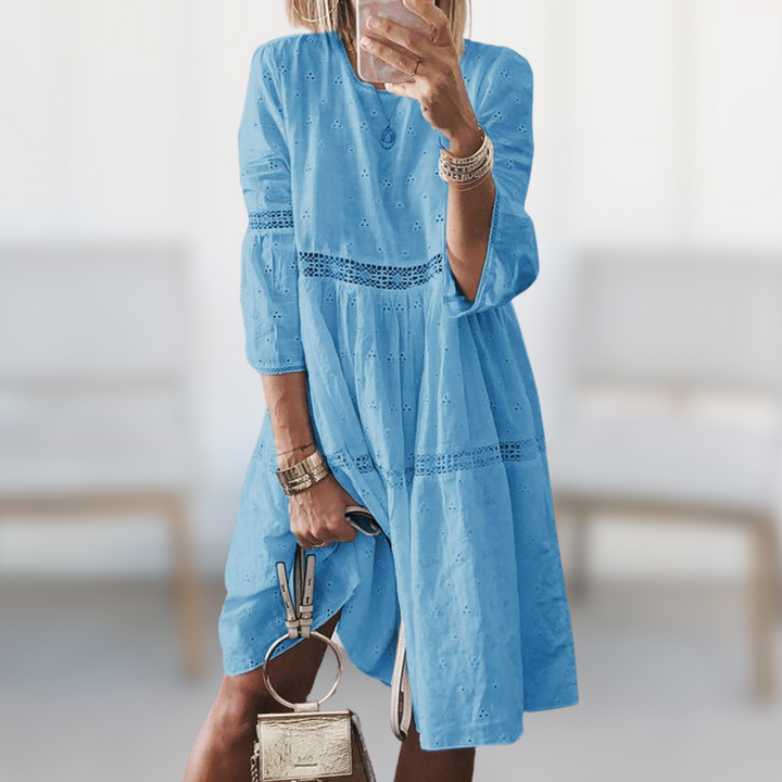 Woman wearing the Majella™ elegant summer dress with a round neckline and flowing silhouette, standing outdoors on a sunny day.