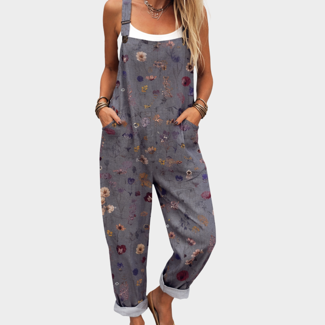 A woman wearing soft grey-blue dungarees with a delicate scattered ditsy floral print and adjustable straps.