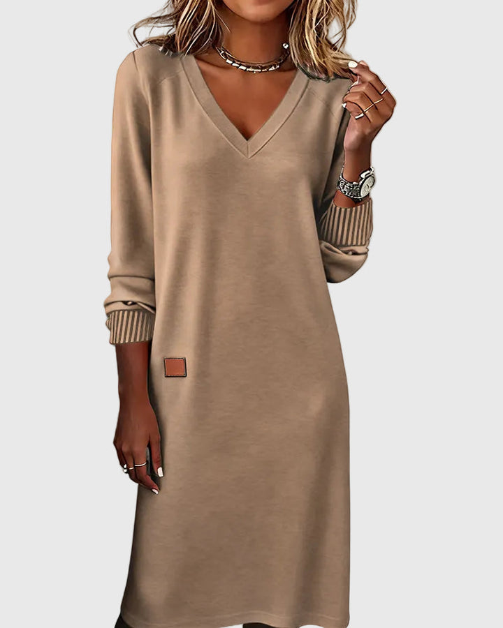 Woman wearing the Emma flowing elegant dress in beige, standing relaxed and smiling.