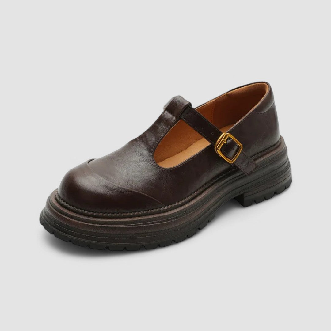 Woman wearing brown Mary Jane comfort shoes with a T-strap, standing on a city footpath.