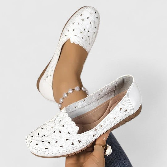A woman wearing white floral cut-out slip-on flats on a warm, sunny day.