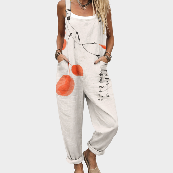 Woman wearing cream dungarees with a painted orange fruit and ink branch print, adjustable straps, calm and relaxed.