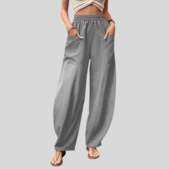 A woman walking in flowing wide-leg trousers with big patch pockets and an elegant, draped silhouette.