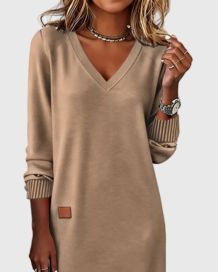 Woman wearing the Emma flowing elegant dress in beige, standing relaxed and smiling.