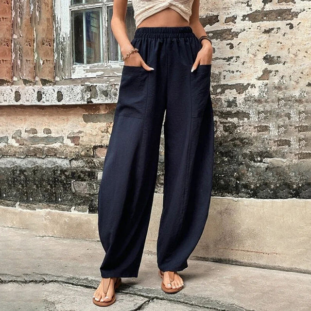 A woman walking in flowing wide-leg trousers with big patch pockets and an elegant, draped silhouette.