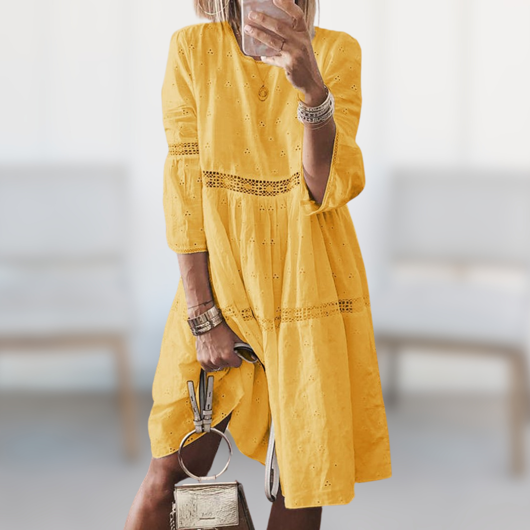 Woman wearing the Majella™ elegant summer dress with a round neckline and flowing silhouette, standing outdoors on a sunny day.
