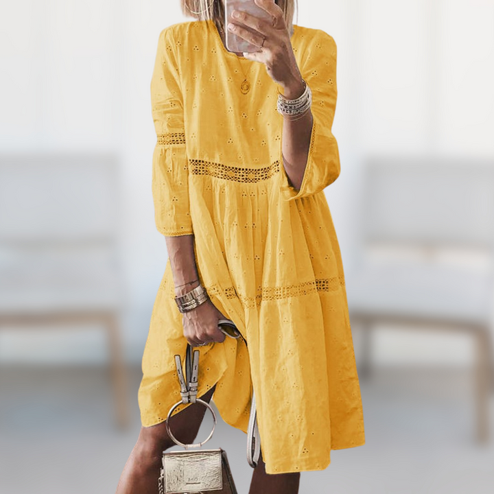 Woman wearing the Majella™ elegant summer dress with a round neckline and flowing silhouette, standing outdoors on a sunny day.