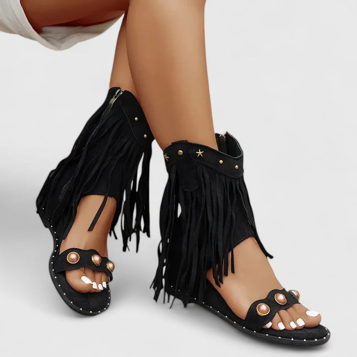 A woman wearing black fringe-detail sandals with a cushioned sole and adjustable strap.