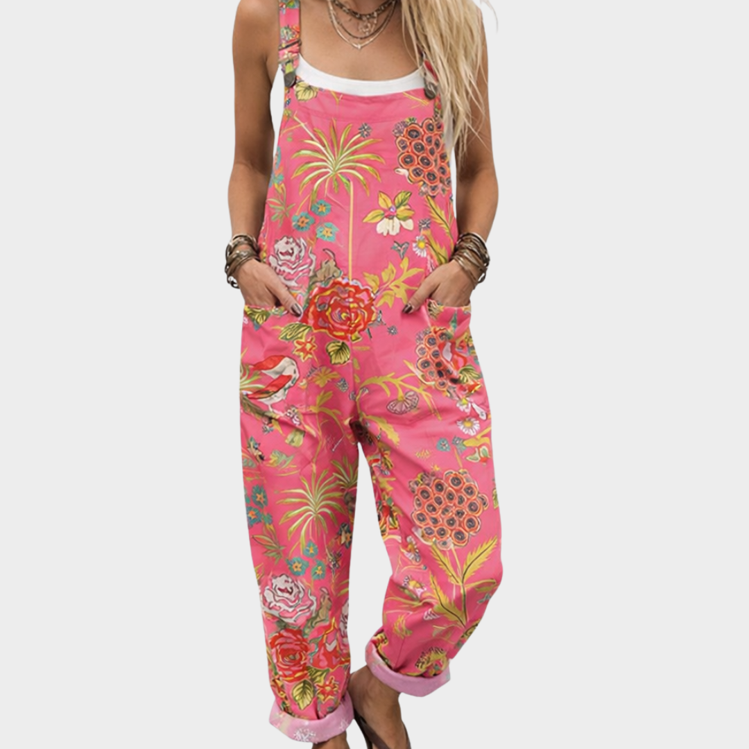 Woman wearing bright coral pink dungarees with a tropical bloom and palm print, adjustable straps, cheerful and relaxed.
