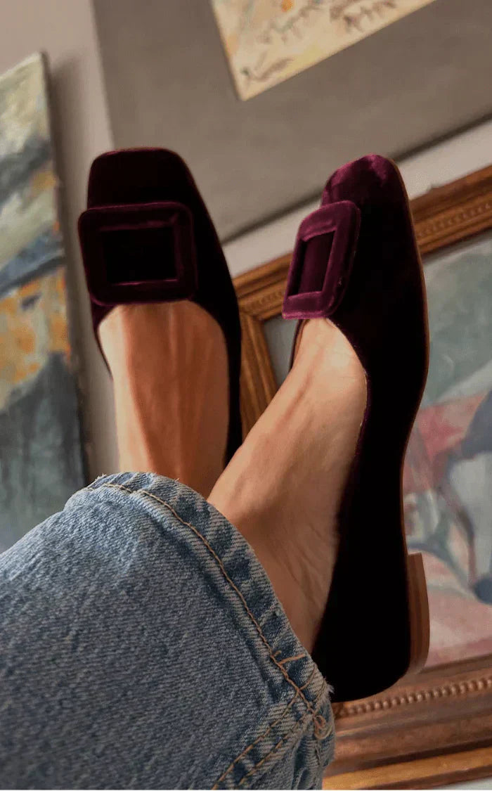 A woman wearing soft, velvety-finish loafers in a rich tone with tailored trousers, looking refined and relaxed.