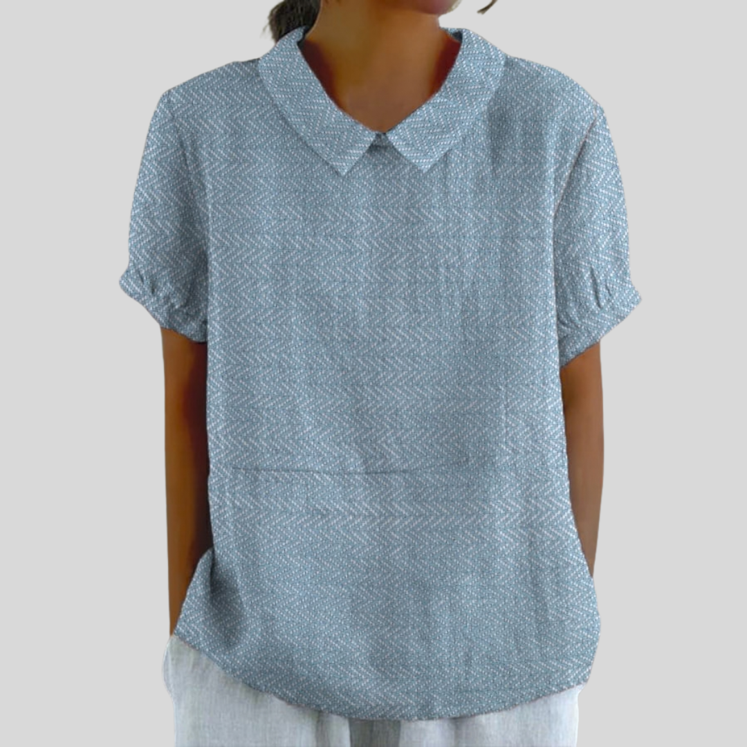A woman wearing a soft blue collared top with a fine texture and refined collar, paired with smart trousers.