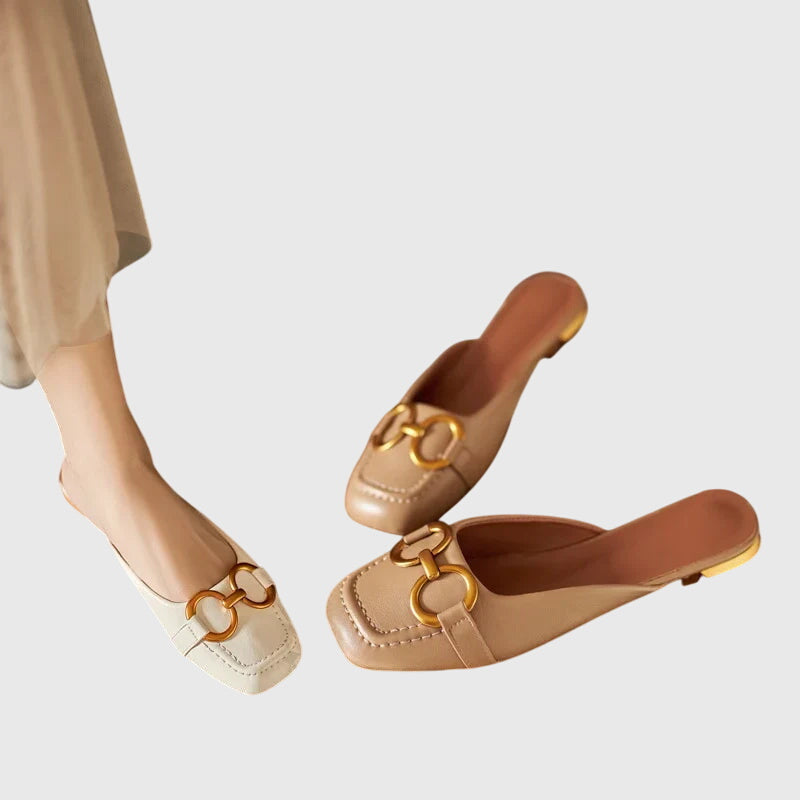 A cream closed-toe mule with a gold horsebit ring detail and a low heel.