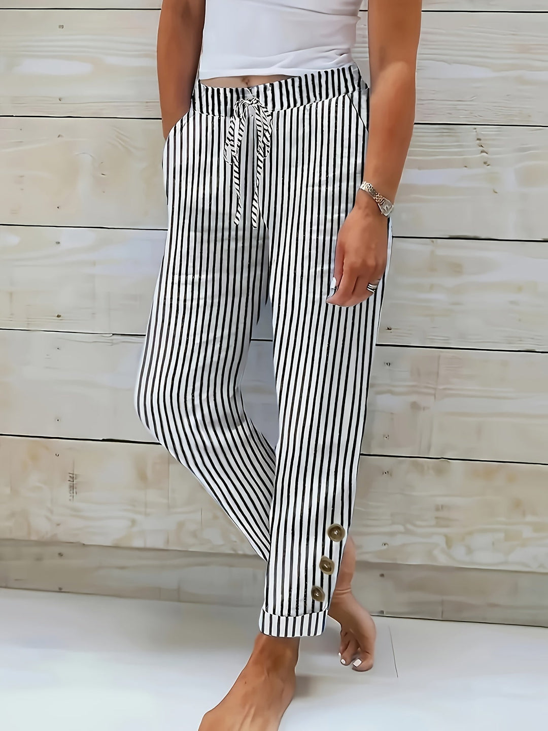 A woman wearing black vertical-striped trousers with a drawstring waist and button hem detail.