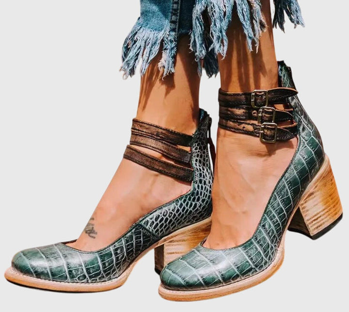 A woman wearing tan block-heel court shoes with buckled ankle straps, walking gracefully in a refined outfit.