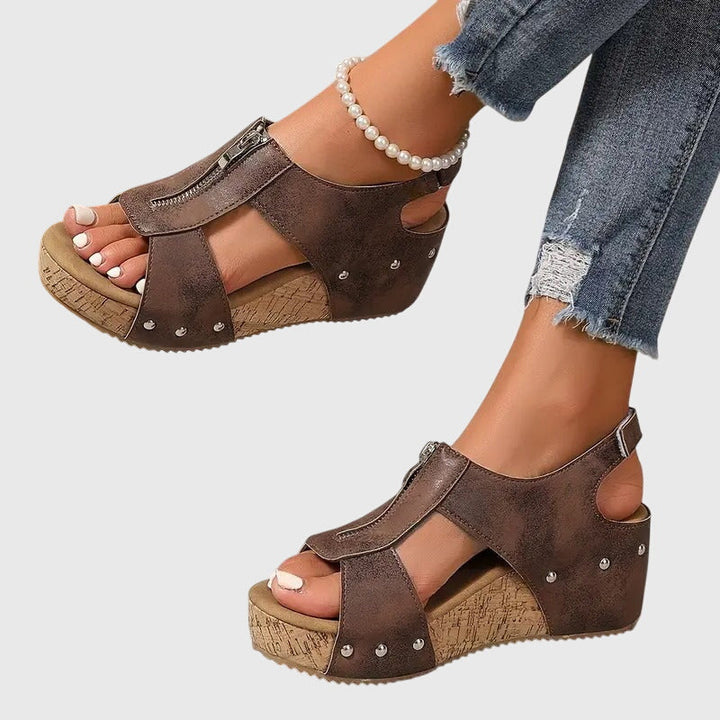 A woman wearing black zip-front wedge sandals with a cushioned footbed and open toe.