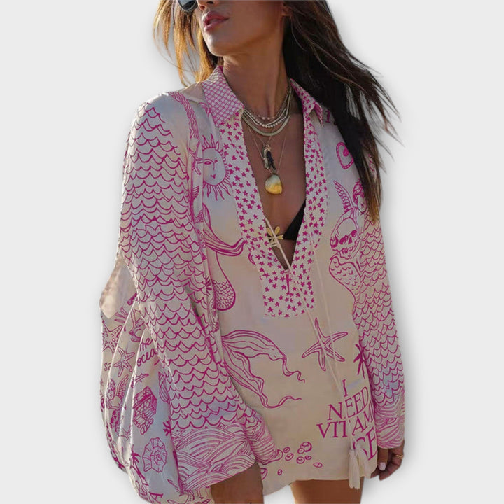 Woman walking on the beach in a relaxed tunic dress with playful maritime print and tie collar.