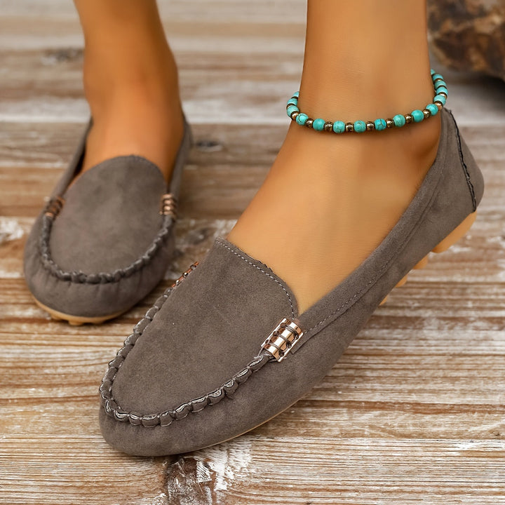 A woman in a ballet-flat loafer stepping lightly along a bright pavement.