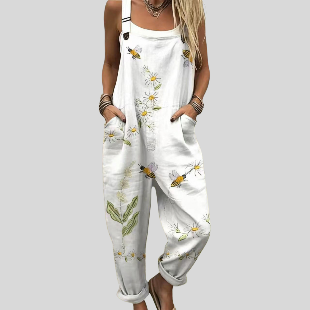 White wide-leg dungarees printed with white daisies, yellow-centred flowers, green leaves and bumblebees on a crisp white ground.