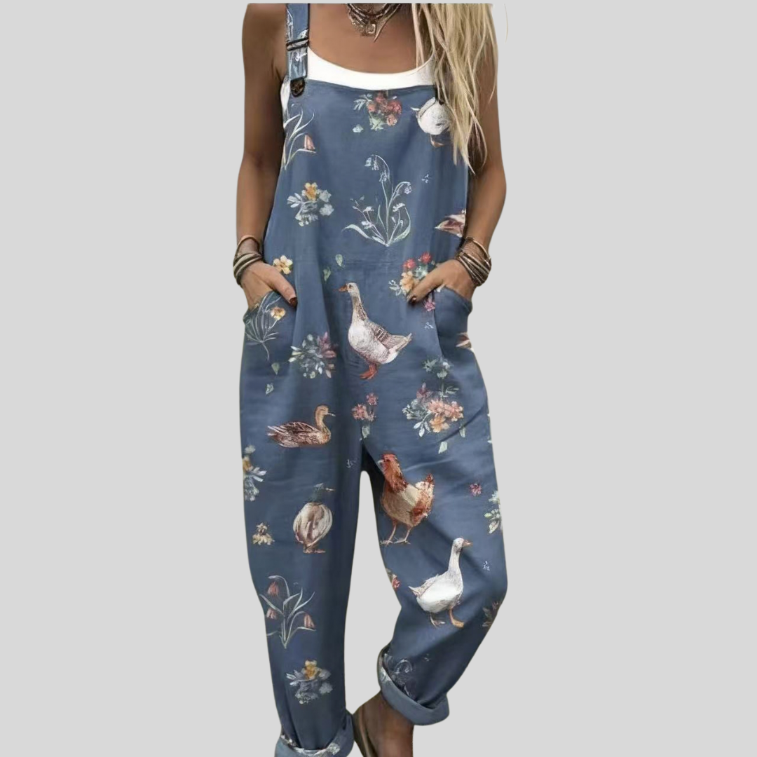 Relaxed wide-leg dungarees in dusty slate blue with a print of hens with red combs, a white goose and flowers among foliage, from Mary Cork Ireland.