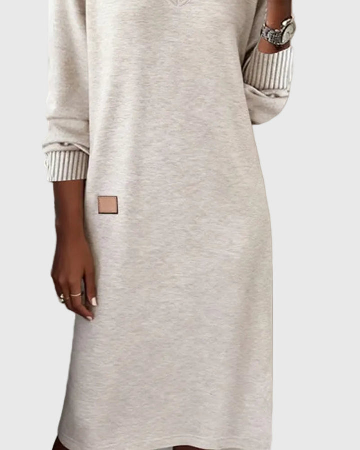 Woman wearing the Emma flowing elegant dress in beige, standing relaxed and smiling.