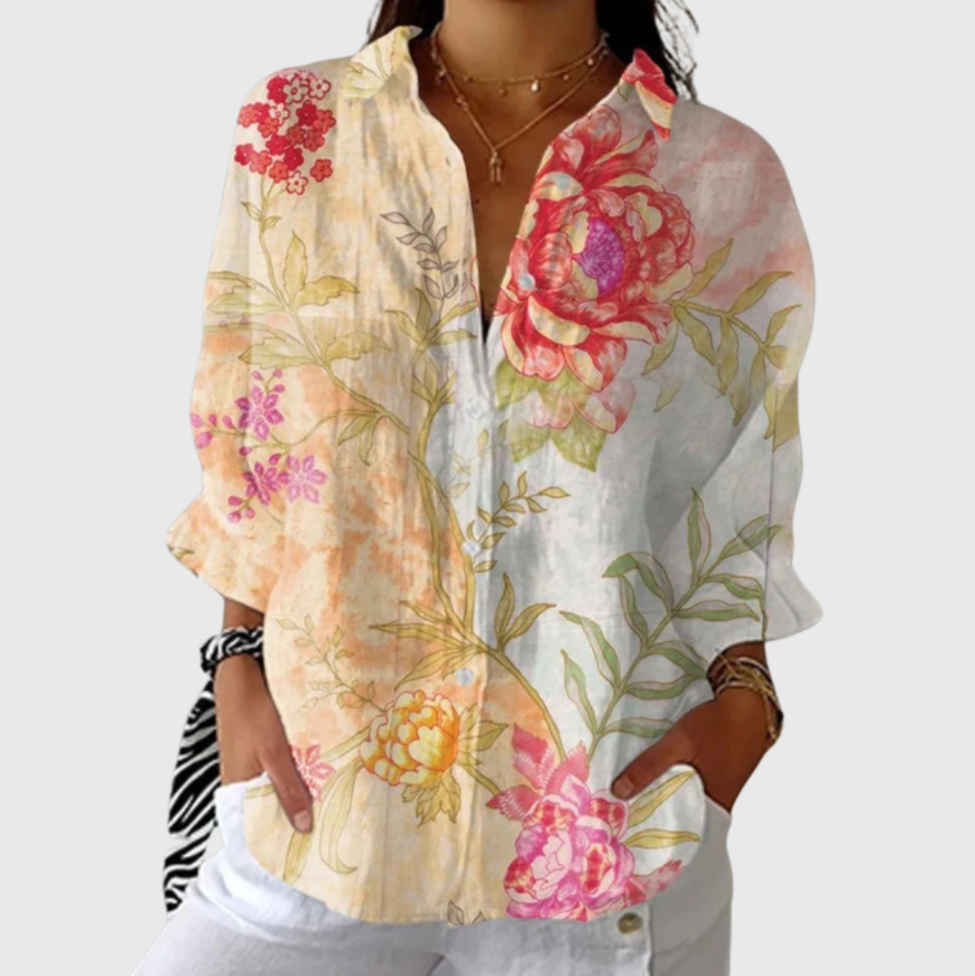 A woman in a colourful floral blouse worn loose with trousers, smiling