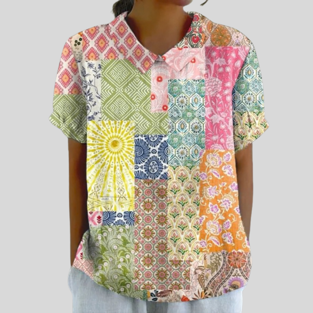 A woman wearing a flowing floral top with a polo collar, looking relaxed and well dressed.